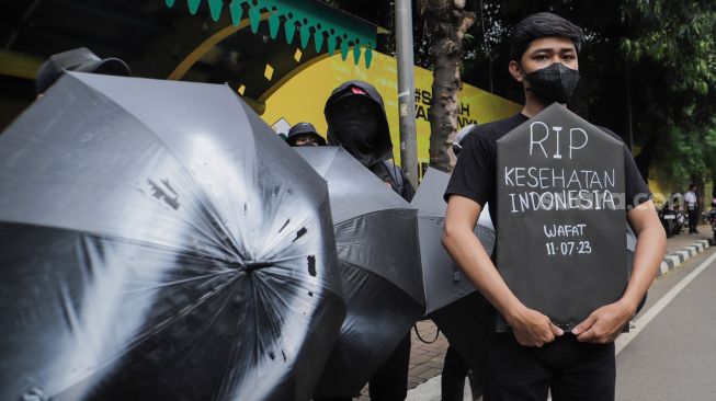 Sejumlah massa saat menggelar aksi unjuk rasa 'Payung Duka' di depan Kementerian Kesehatan, Jakarta, Jumat (14/7/2023). [Suara.com/Alfian Winanto]