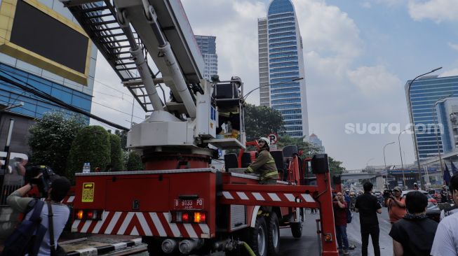 Petugas Damkar melakukan pendinginan videotron yang terbakar di Menara K-Link, Jakarta, Sabtu (15/7/2023). [Suara.com/Alfian Winanto]