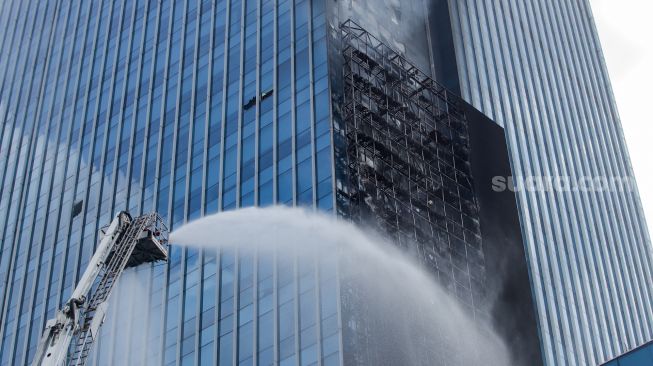 Petugas Damkar melakukan pendinginan videotron yang terbakar di Menara K-Link, Jakarta, Sabtu (15/7/2023). [Suara.com/Alfian Winanto]