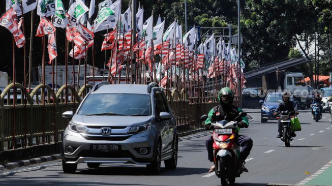 Pengendara melintas di dekat bendera parpol yang terpasang di pembatas jalan kawasan Tebet, Jakarta, Selasa (18/7/2023). [Suara.com/Alfian Winanto]