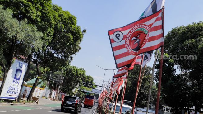 Pengendara melintas di dekat bendera parpol yang terpasang di pembatas jalan kawasan Tebet, Jakarta, Selasa (18/7/2023). [Suara.com/Alfian Winanto]