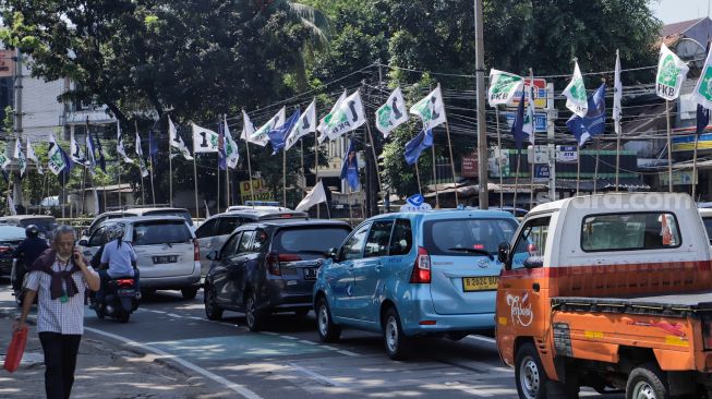 Pengendara melintas di dekat bendera parpol yang terpasang di pembatas jalan kawasan Tebet, Jakarta, Selasa (18/7/2023). [Suara.com/Alfian Winanto]