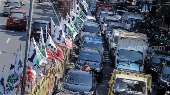 Pengendara melintas di dekat bendera parpol yang terpasang di pembatas jalan kawasan Tebet, Jakarta, Selasa (18/7/2023). [Suara.com/Alfian Winanto]