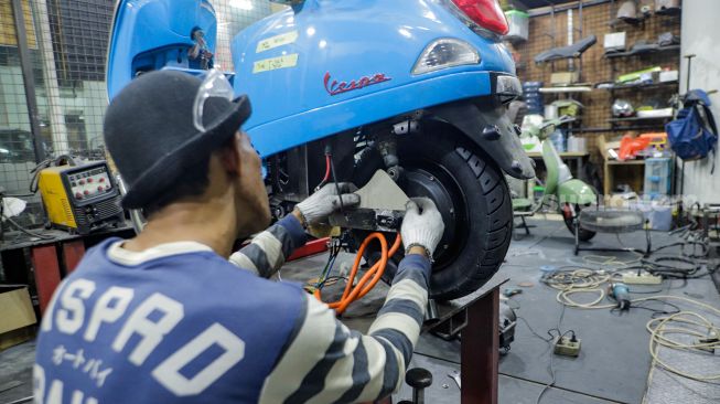 Pekerja mengkonversi vespa klasik menjadi vespa listrik di bengkel Elders Garage, Gedung Smesco Jakarta, Kamis (28/7/2022). [Suara.com/Alfian Winanto]