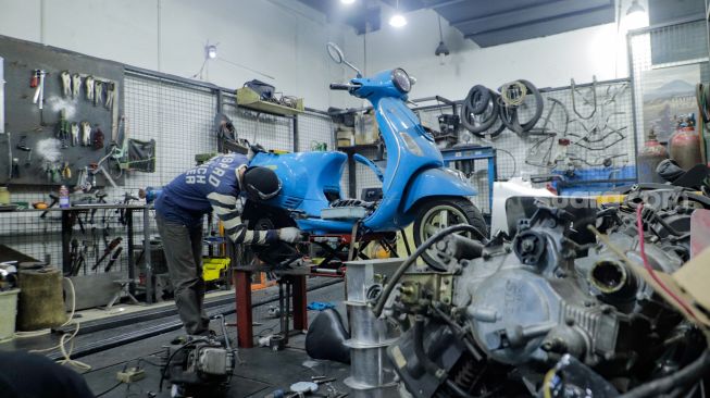 Pekerja mengkonversi vespa klasik menjadi vespa listrik di bengkel Elders Garage, Gedung Smesco Jakarta, Kamis (28/7/2022). [Suara.com/Alfian Winanto]