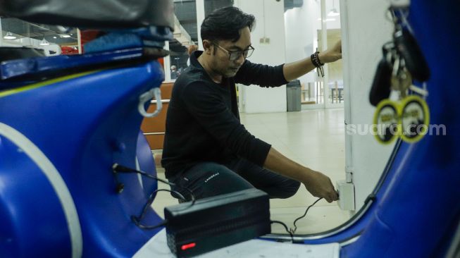 Pekerja mencoba mengisi daya vespa klasik yang sudah dikonversi menjadi vespa listrik di bengkel Elders Garage, Gedung Smesco Jakarta, Kamis (28/7/2022). [Suara.com/Alfian Winanto]