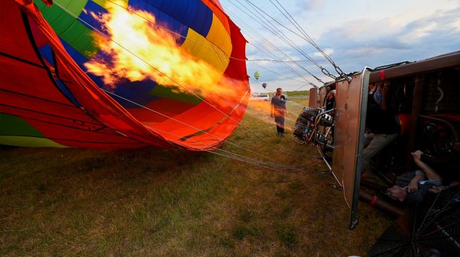 Peserta memanaskan balon udara untuk diterbangkan di pangkalan udara Chambley-Bussieres saat festival balon udara internasional ke-18 "Grand-Est Mondial Air Ballons" di Hageville, Prancis, Jumat (21/7/2023). [Jean-Christophe VERHAEGEN / AFP]
