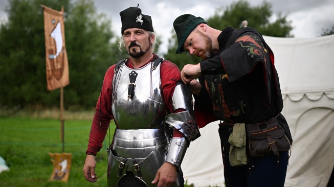 Peserta bersiap menggunakan baju zirah untuk berkompetisi dalam acara jousting Joust Legendaris di Kastil Kenilworth, Coventry, Inggris, Sabtu (29/7/2023). [Oli SCARFF / AFP]