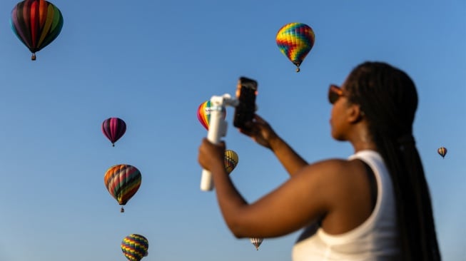 Seorang penonton memotret balon udara yang terbang selama Festival Balon Tahunan New Jersey ke-40 di Bandara Solberg, Readington, New Jersey, Jumat (28/7/2023). [Julia Nikhinson / AFP]
