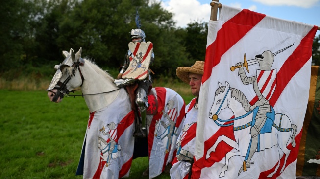 Peserta mengendarai kudanya bersama pengawalnya untuk berkompetisi dalam acara jousting Joust Legendaris di Kastil Kenilworth, Coventry, Inggris, Sabtu (29/7/2023). [Oli SCARFF / AFP]