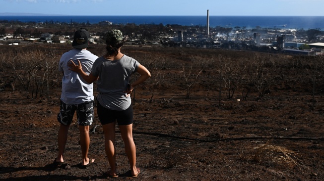 Penduduk Maui melihat pemandangan kota yang hancur  akibat kebakaran hutan hebat yang melanda di Lahaina, Maui barat, Hawaii, Jumat (11/8/2023). [Patrick T. Fallon / AFP]