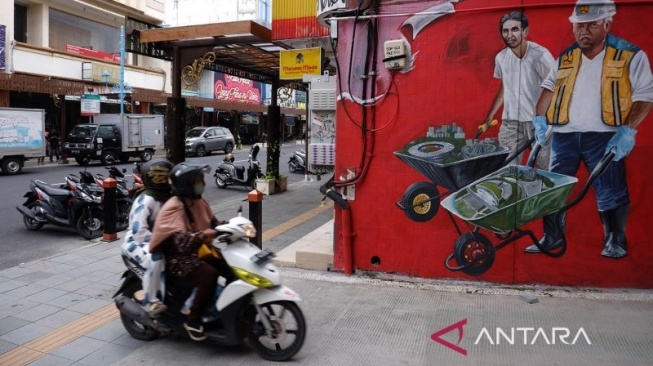 Warga melintasi gambar mural yang menghiasi Koridor Gatot Subroto (Gatsu) hingga Ngarsopuro seusai revitalisasi penataan kawasan setempat di Solo, Jawa Tengah, Selasa (3/1/2023).ANTARA FOTO/Maulana Surya/aww]