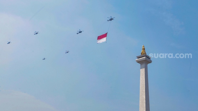 Helikopter membawa bendera merah putih melintas di Jakarta, Kamis (17/8/2023). [Suara.com/Alfian Winanto]