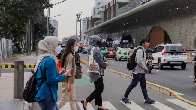 Masyarakat berjalan sambil menggunakan masker di Jalan MH Thamrin, Jakarta, Senin (21/8/2023). [Suara.com/Alfian Winanto]