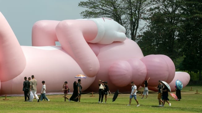 Pengunjung melihat instalasi seni dari yang dibuat oleh seniman dunia Brian Donnelly atau KAWS saat pameran bertajuk KAWS:HOLIDAY Indonesia di pelataran Candi Brahma di Kompleks Candi Prambanan, Sleman, Yogyakarta, Sabtu (19/8/2023).   [DEVI RAHMAN / AFP]