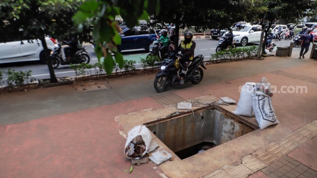 Pengendara motor menghindari lubang saluran kabel di Jalan Raya Casablanca, Jakarta, Jumat (25/8/2023). [Suara.com/Alfian Winanto]