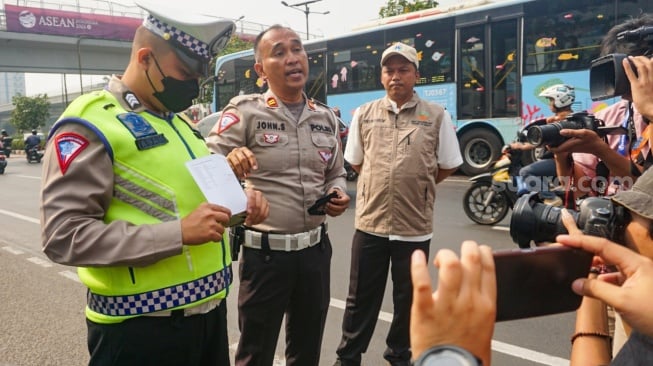 Polisi memberikan pengarahan kepada pengendara mobil yang akan melakukan uji emisi di Subdit Gakkum Ditlantas Polda Metro Jaya, Jakarta, Jumat (1/9/2023). [Suara.com/Alfian Winanto]