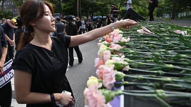 Seorang pengunjuk rasa meletakkan bunga di atas panggung untuk memperingati seorang guru sekolah dasar yang meninggal karena bunuh diri pada bulan Juli lalu saat unjuk rasa menuntut perlindungan hak-hak guru di depan Majelis Nasional di Seoul, Korea Selatan, Senin (4/9/2023). [Yung Yeon-je / AFP]