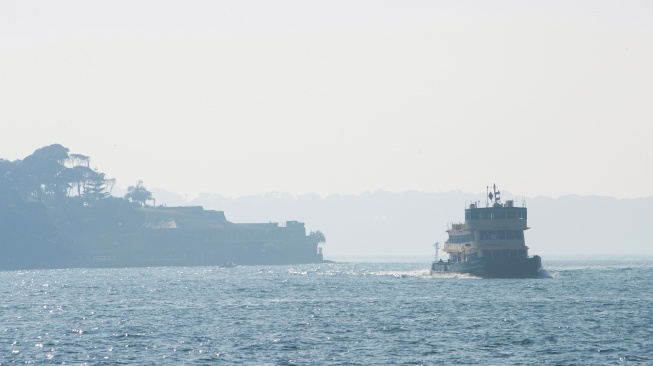 Sebuah kapal feri melintasi pelabuhan yang diselimuti kabut asap di Sydney, Australia, Rabu (13/9/2023). [Steve CHRISTO / AFP]