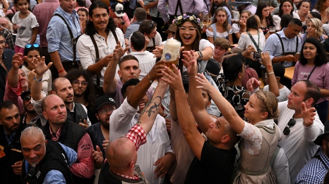 Orang-orang saling bersulang saat merayakan pembukaan festival Oktoberfest 2023 di Munich, Jerman, Sabtu (16/9/2023). [Christof STACHE / AFP]