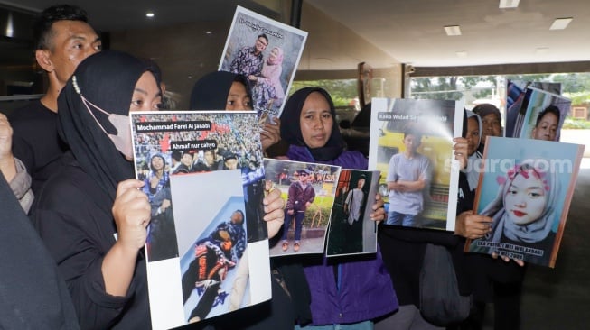 Keluarga Korban Tragedi Kanjuruhan menunjukkan poster berisi foto keluarga mereka yang menjadi korban saat mendatangi Bareskrim Mabes Polri, Jakarta, Rabu (27/9/2023). [Suara.com/Alfian Winanto]