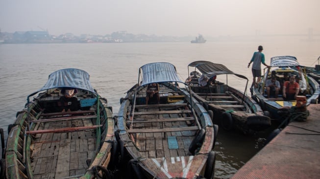 Sejumlah pengemudi perahu tradisional menunggu calon penumpang dengan latar belakang sungai musi yang tertutup kabut asap di Palembang, Sumatera Selatan, Sabtu (7/10/2023). [ANTARA FOTO/Nova Wahyudi/YU]
