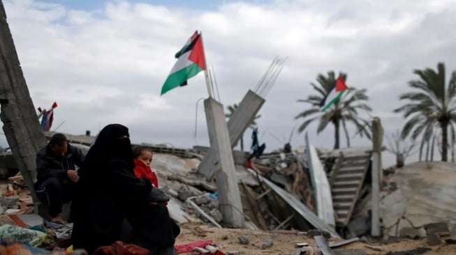 Anggota keluarga Palestina duduk di lokasi rumah mereka yang hancur, pada sebuah hari musim dingin di selatan Jalur Gaza. [REUTERS/Mohammed Salem/wsj/cfo (REUTERS/MOHAMMED SALEM]