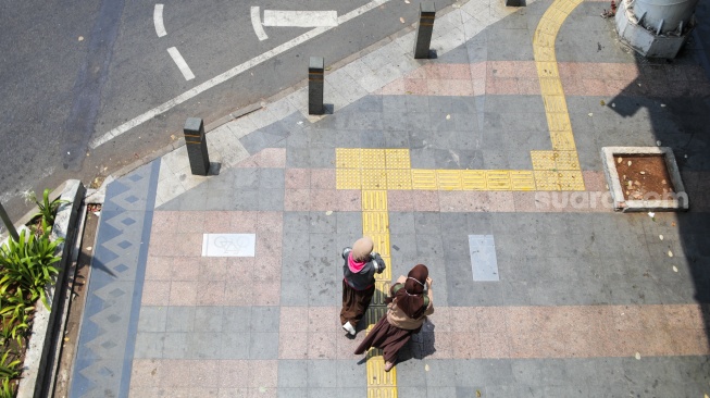 Pekerja melintasi pelican crossing di Jakarta, Senin (9/10/2023). [Suara.com/Alfian Winanto]