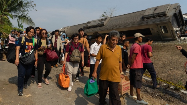 Penumpang membawa barang bawaan mereka di dekat gerbong kereta api yang anjlok akibat kecelakaan di kawasan Kalimenur, Sukoreno, Kulonprogo, D.I Yogyakarta, Selasa (17/10/2023). [ANTARA FOTO/Andreas Fitri Atmoko].