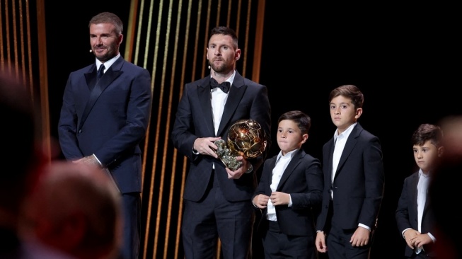 Penyerang Inter Miami asal Argentina, Lionel Messi (tengah) bereaksi dengan trofinya di samping anak-anaknya di atas panggung saat ia menerima penghargaan Ballon d'Or 2023 yang diberikang langsung oleh eks pemain Manchester United dan salah satu pemilik Inter Miami David Beckham (kiri) dalam Upacara penghargaan Ballon d'Or 2023 di Theatre du Chatelet di Paris pada 30 Oktober 2023.FRANCK FIFE / AFP.