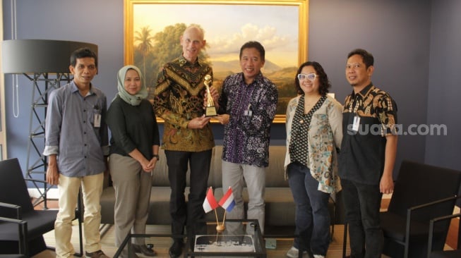 Duta Besar (Dubes) Belanda Lambert Grijns saat menerima piala Apresiasi Local Media Summit (LMS) 2023 dari Pemimpin Redaksi Suara.com, Suwarjono, berpose bersama rombongan tamu dari International Media Support (IMS) dan Suara.com beserta stafnya, di ruangan Kedubes Belanda, Jakarta, Jumat (3/11/2023). [Suara.com/Adit Rianto]