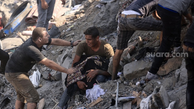 Seorang menggendong jenazah ibunya yang terbungkus selimut di tengah reruntuhan bangunan yang hancur dalam serangan Israel di kamp pengungsi Bureij di Jalur Gaza, Palestina, Kamis (2/11/2023).  [MAHMUD HAMS/AFP]