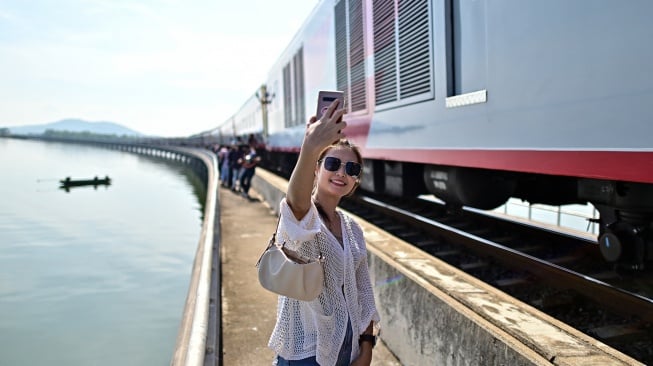 Seorang wisatawan berswafoto saat menaiki wisata "Kereta Apung" yang tengah berhenti di Bendungan Pasak Jolasid, Provinsi Lopburi, Thailand, Sabtu (4/11/2023). [MANAN VATSYAYANA / AFP]