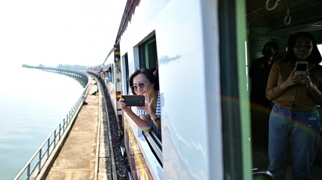 Seorang wisatawan mengabadikan pemandangan saat menaiki wisata "Kereta Apung" yang tengan melintas di Bendungan Pasak Jolasid, Provinsi Lopburi, Thailand, Sabtu (4/11/2023). [MANAN VATSYAYANA / AFP]