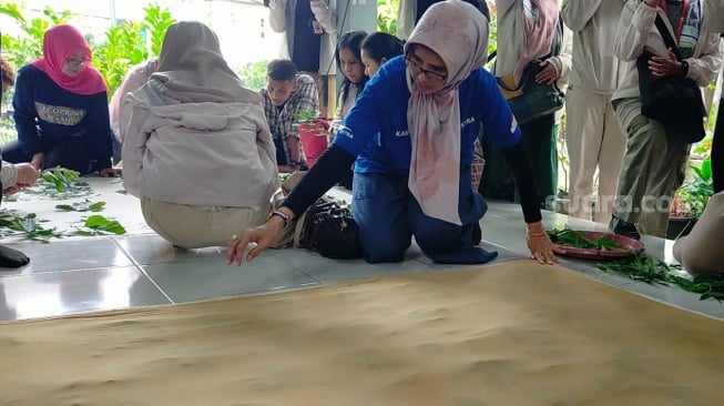 Proses pemberian pola di atas kain dengan daun kemudian ditutup kain penggulung dalam Workshop Wartawan Lingkungan 2023 oleh Astra di KBA Pekayon Bekasi [Suara.com/CNR ukirsari].