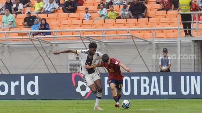 Pesepak bola Timnas Spanyol U-17 Quim Junyent berebut bola dengan pemain Timnas Jerman U-17 Bilal Yancinkaya pada pertandingan babak Perempat Final Piala Dunia U-17 2023 di Jakarta International Stadium (JIS), Jakarta, Jumat (24/11/2023). [Suara.com/Alfian Winanto]
 