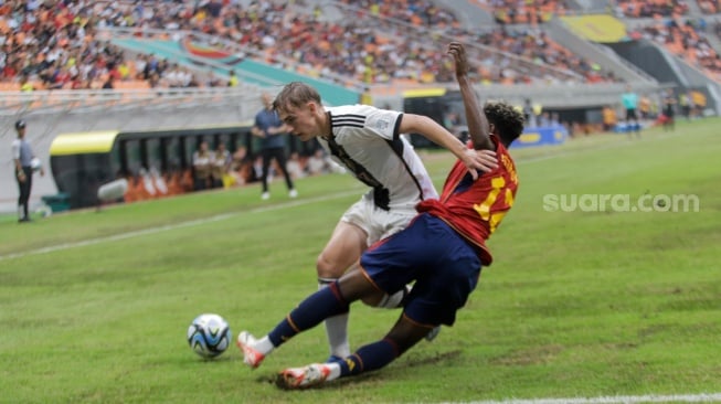 Pesepak bola Timnas Jerman U-17 Maximilian Henning berebut bola dengan pemain Timnas Spanyol U-17 Igor Oyono pada pertandingan babak Perempat Final Piala Dunia U-17 2023 di Jakarta International Stadium (JIS), Jakarta, Jumat (24/11/2023). [Suara.com/Alfian Winanto]
 