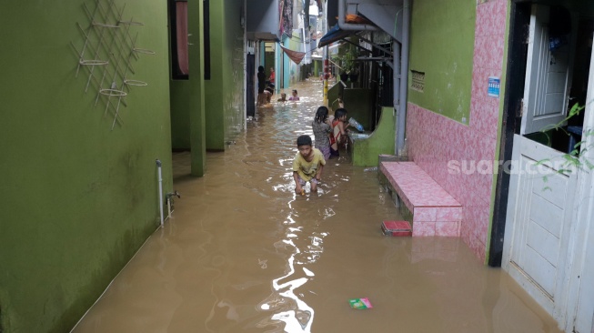 Warga melintasi banjir yang melanda di kawasan Kebon Pala, Kampung Melayu, Jakarta, Kamis (30/11/2023). [Suara.com/Alfian Winanto]