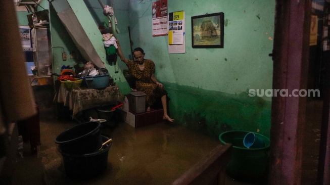 Warga beristirahat di rumahnya yang tergenang banjir di kawasan Kebon Pala, Kampung Melayu, Jakarta, Kamis (30/11/2023). [Suara.com/Alfian Winanto]