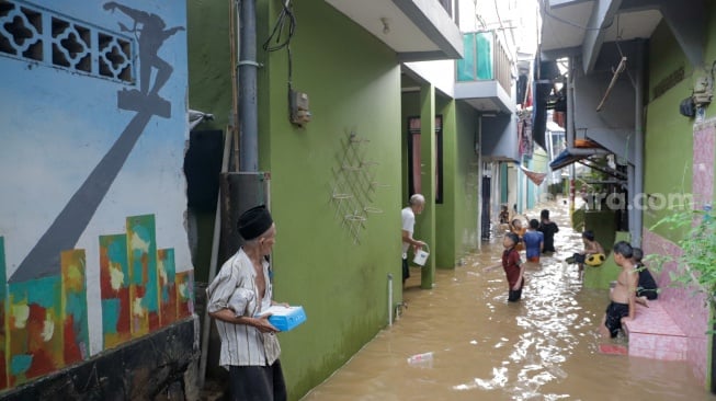 Warga melintasi banjir yang melanda di kawasan Kebon Pala, Kampung Melayu, Jakarta, Kamis (30/11/2023). [Suara.com/Alfian Winanto]