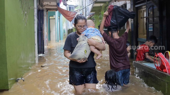 Warga melintasi banjir yang melanda di kawasan Kebon Pala, Kampung Melayu, Jakarta, Kamis (30/11/2023). [Suara.com/Alfian Winanto]