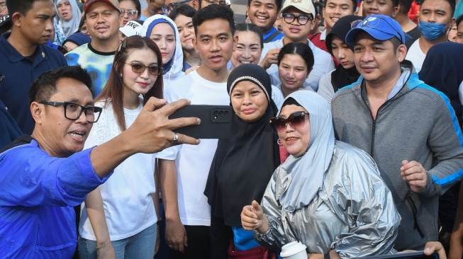 Cawapres nomor urut 2 Gibran Rakabuming Raka (tengah) bersama istrinya Selvi Ananda (kedua kiri) dan sejumlah politisi dari partai politik pengusung Gibran berswa foto dengan warga di area hari bebas kendaraan bermotor (HBKB) Jalan MH Thamrin, Jakarta, Minggu (3/12/2023). Dalam kesempatan tersebut Gibran menyapa warga yang sedang berolah raga saat HBKB atau 'car free day' (CFD) dan membagikan susu ke anak-anak. ANTARA FOTO/Aditya Pradana Putra/rwa.