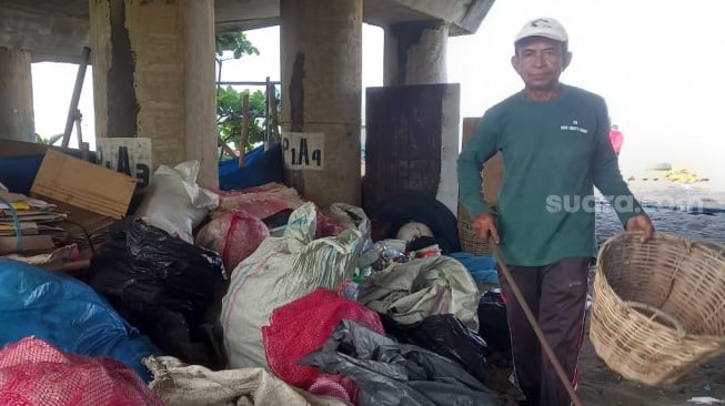 Abadi sedang di bawah jembatan ujung jalur dua Pantai Padang, tempat ia dan anggota KUB Saiyo Sakato Mandiri mengeringkan sampah-sampah yang telah dipilah usai dikumpulkan dari pinggir laut. [Suara.com/Riki Chandra]