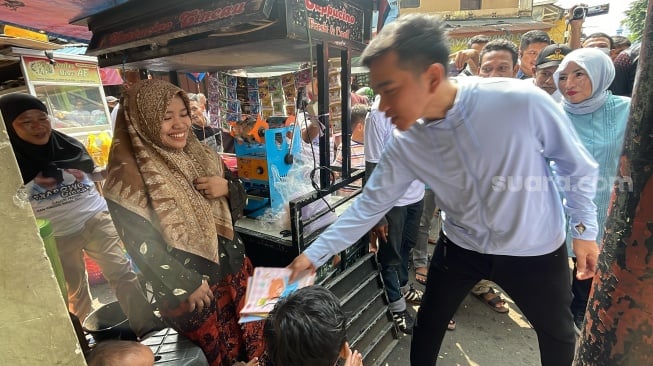 Calon wakil presiden nomor urut 2, Gibran Rakabuming Raka memberikan buku untuk anak-anak saat blusukan di Pasar Rumput, Jakarta Selatan, Senin (11/12/2023). (Suara.com/Novian)