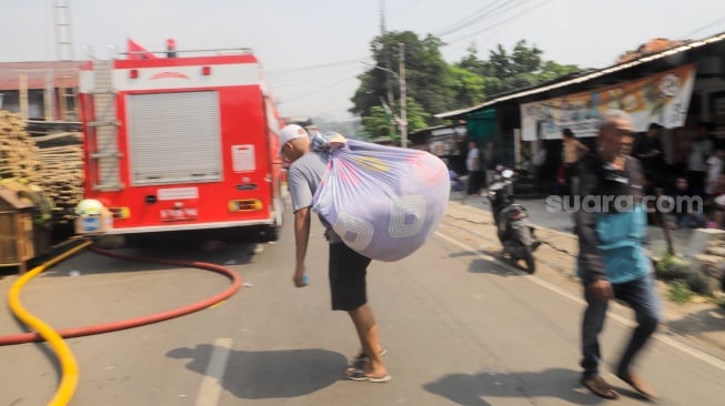 Warga mengevakuasi barang berharga saat kebakaran membakar pekukiman padat di kawasan Manggarai, Tebet, Jakarta, Kamis (14/12/2023). [Suara.com/Alfian Winanto]