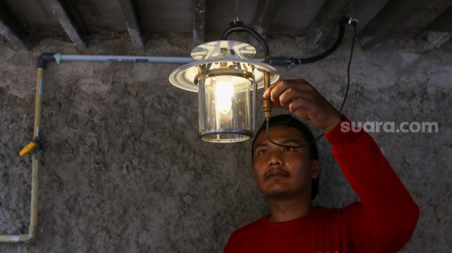 Pekerja menyalakan lampu yang menggunakan energi dari limbah kotoran ternak di kawasan Pancoran, Jakarta, Jumat (15/12/2023). [Suara.com/Alfian Winanto]