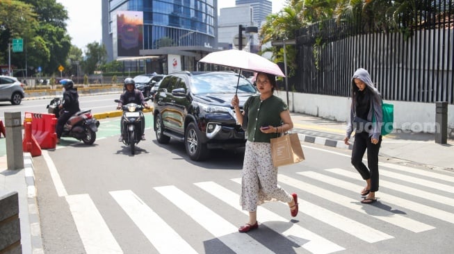 Pekerja melindungi tubuh dari terik matahari menggunakan payung saat berjalan di kawasan Sudirman, Jakarta, Kamis (21/12/2023). [Suara.com/Alfian Winanto]