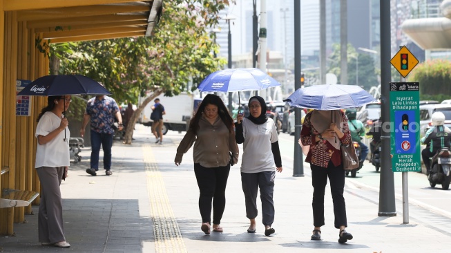 Pekerja melindungi tubuh dari terik matahari menggunakan payung saat berjalan di kawasan Sudirman, Jakarta, Kamis (21/12/2023). [Suara.com/Alfian Winanto]