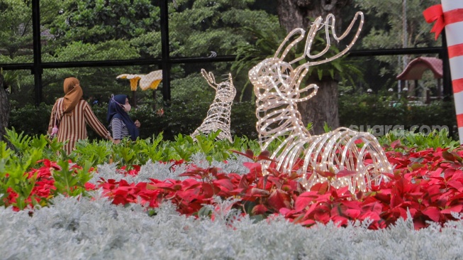 Sejumlah warga menghabiskan waktu liburan dengan bermain dan berfoto di depan dekorasi khas Natal di Taman Lapangan Banteng, Jakarta, Selasa (26/12/2023). [Suara.com/Alfian Winanto]