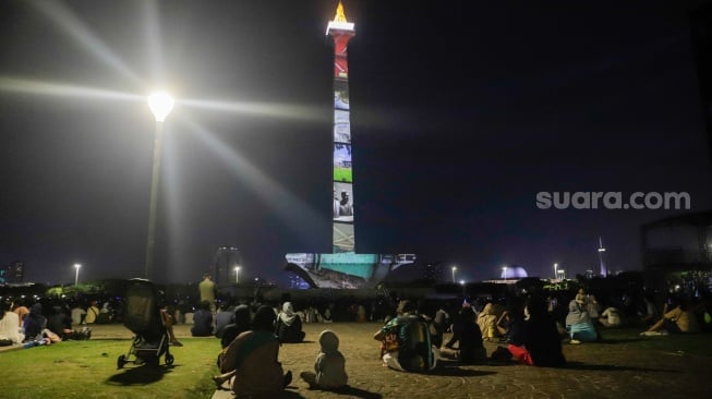 Pengunjung menyaksikan pertunjukan video mapping Monas Week di Monumen Nasional (Monas), Jakarta, Jumat (29/12/2023). [Suara.com/Alfian Winanto]